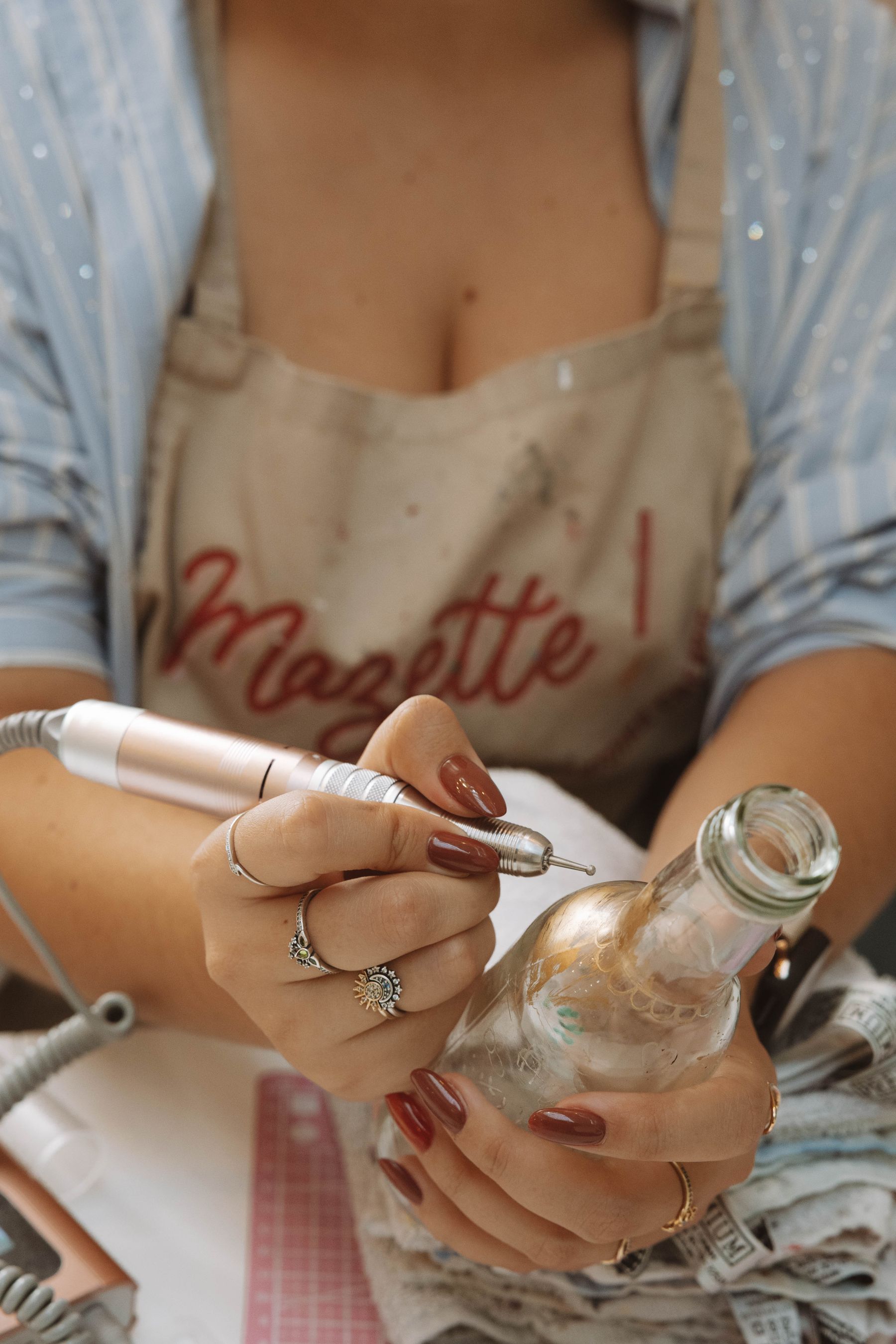 An artisan working a fine engraving tool against the surface of a glass bottle
