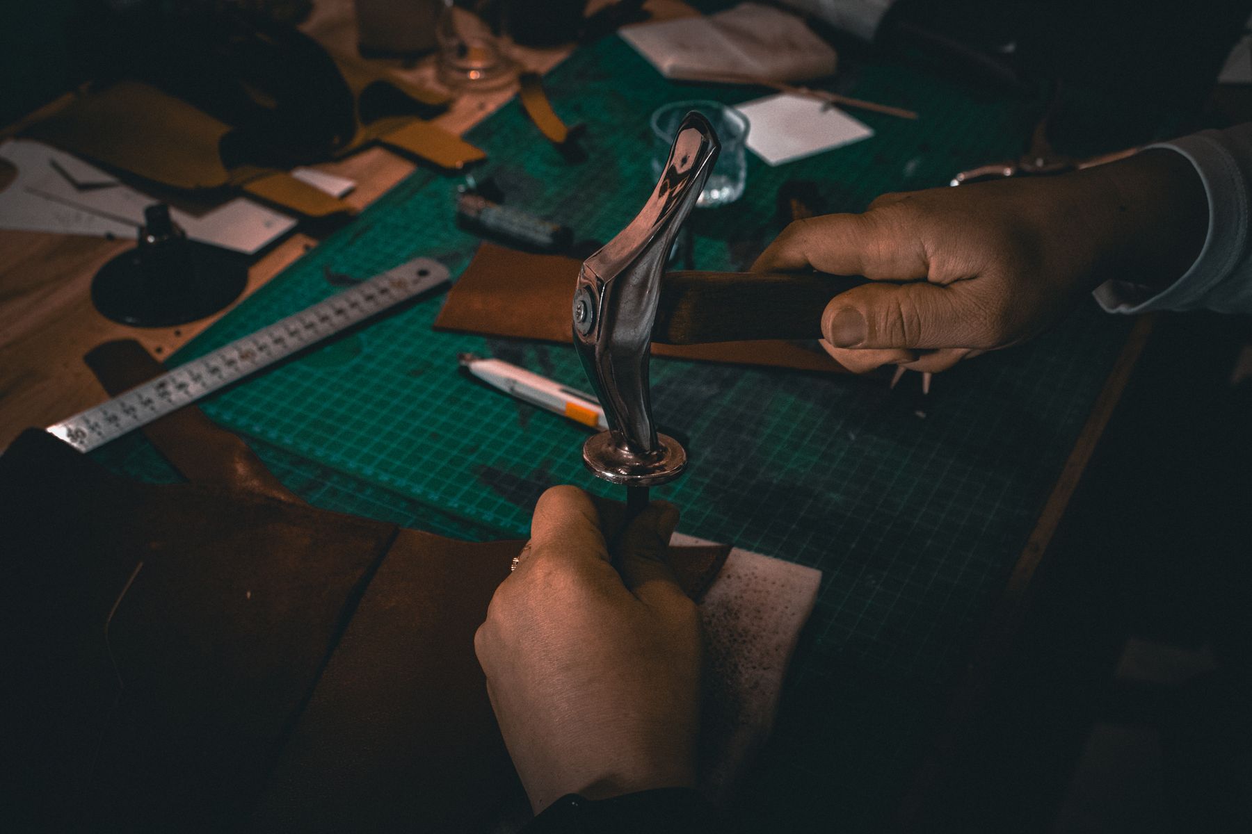 A leatherworker shaping dark leather by hand at a tool-covered bench