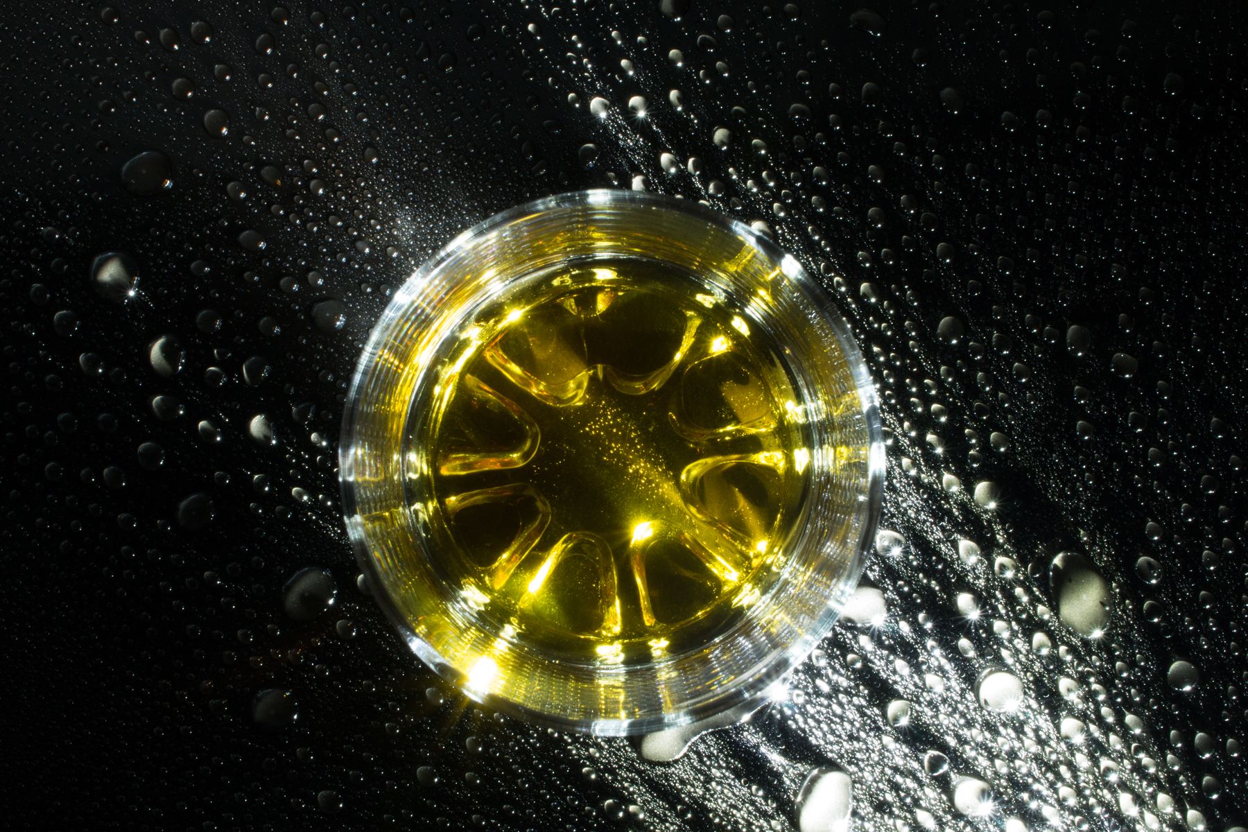 A top view of whisky and ice on a wet dark surface